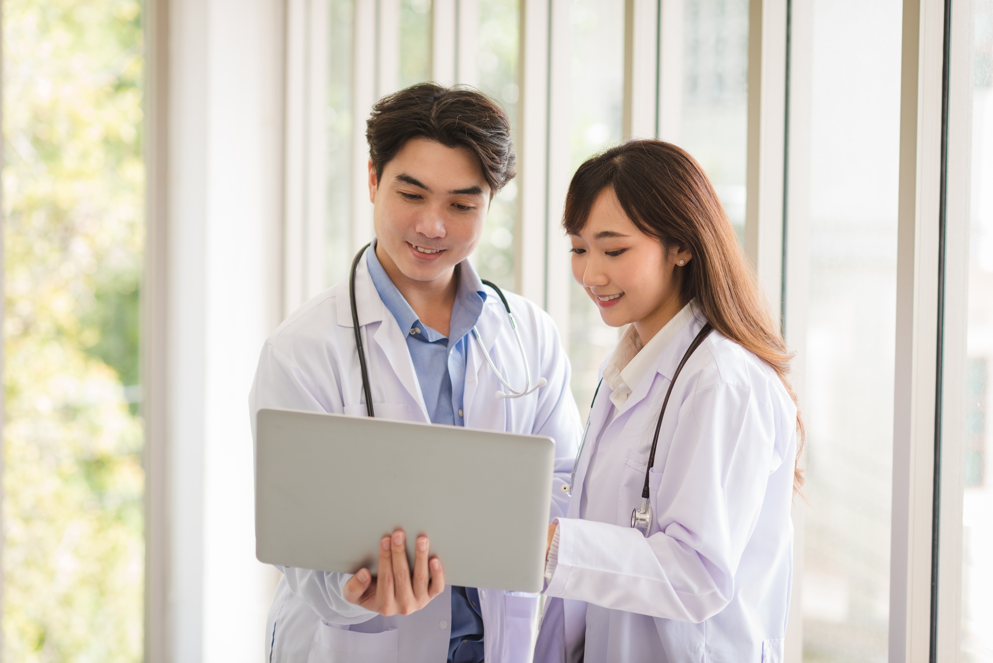 Group of Asian doctors team portrait standing and using laptop with other colleagues in background.